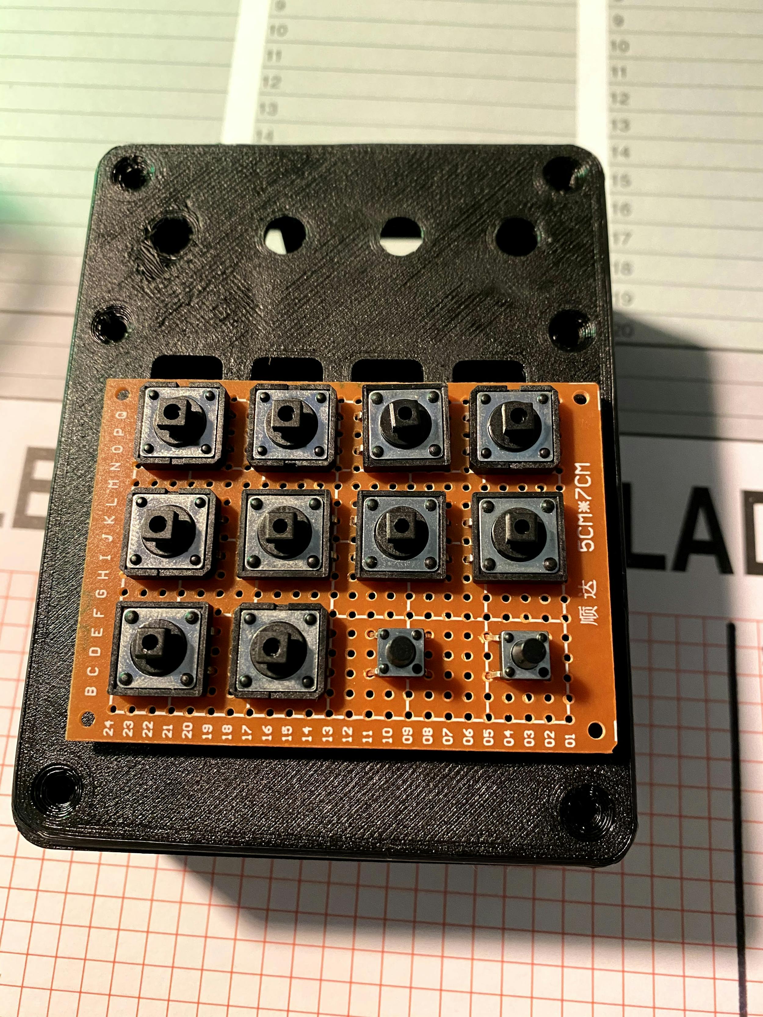 A 3 by 4 grid of buttons, lined up on protoboard to start prototyping the build